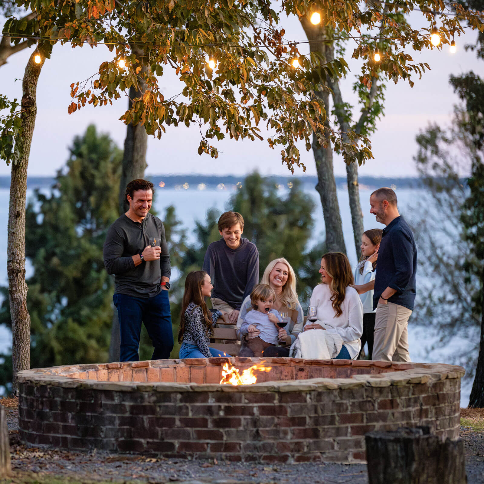A group of people enjoy a firepit-side chat during sunset on the shore of Ross Barnett Reservoir.