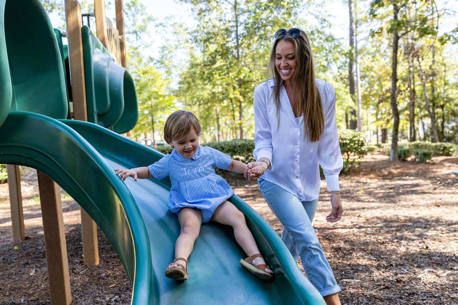 A woman holds a child's hand while they go down a slide on the community playground.